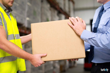 Warehouse worker and manager help each other move a cardboard box.